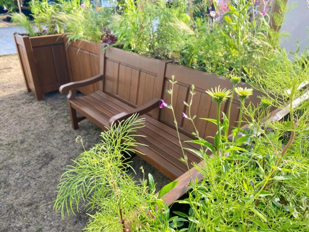 Two wooden benches integrated into raised timber planters, with vibrant flowering plants spilling over the edges at the RHS show.