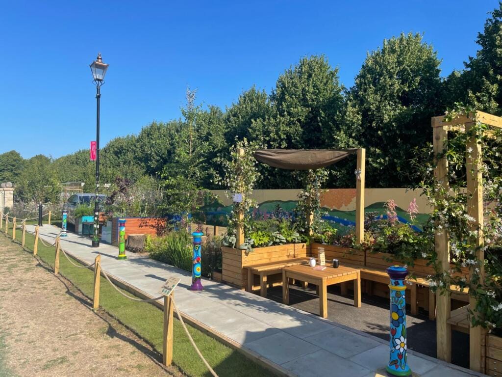 A neighbouring installation at RHS Hampton Court showing colourful street furniture, a painted mural, and a pedestrian-friendly path lined with rope barriers.